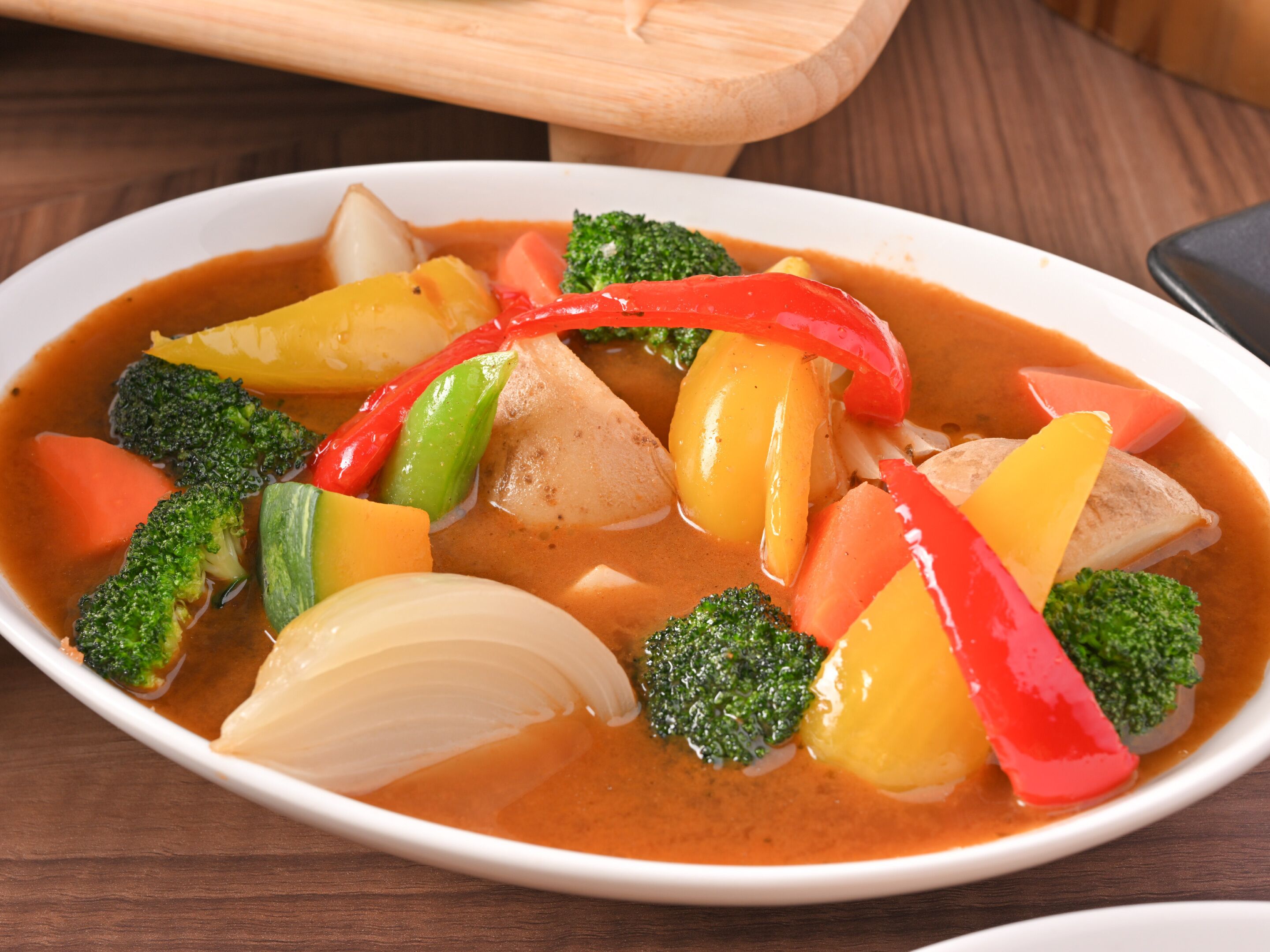 Un tazón de sopa de verduras con brócoli, pimientos rojos y papas.