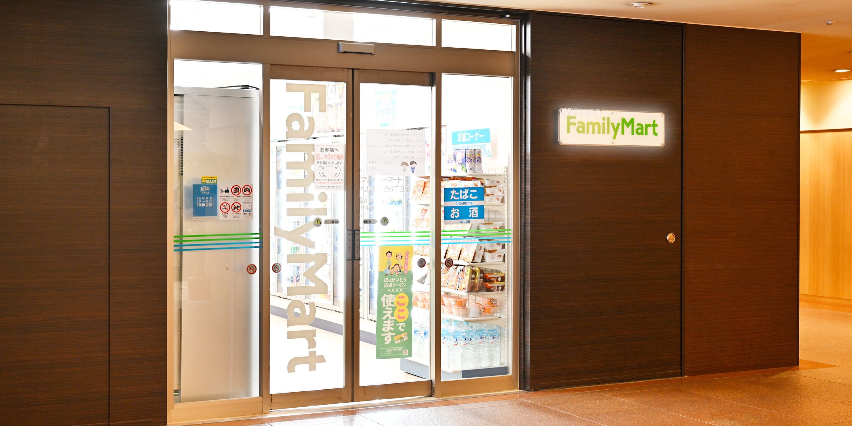 A FamilyMart entrance with glass doors, a sign, and a display of products inside.