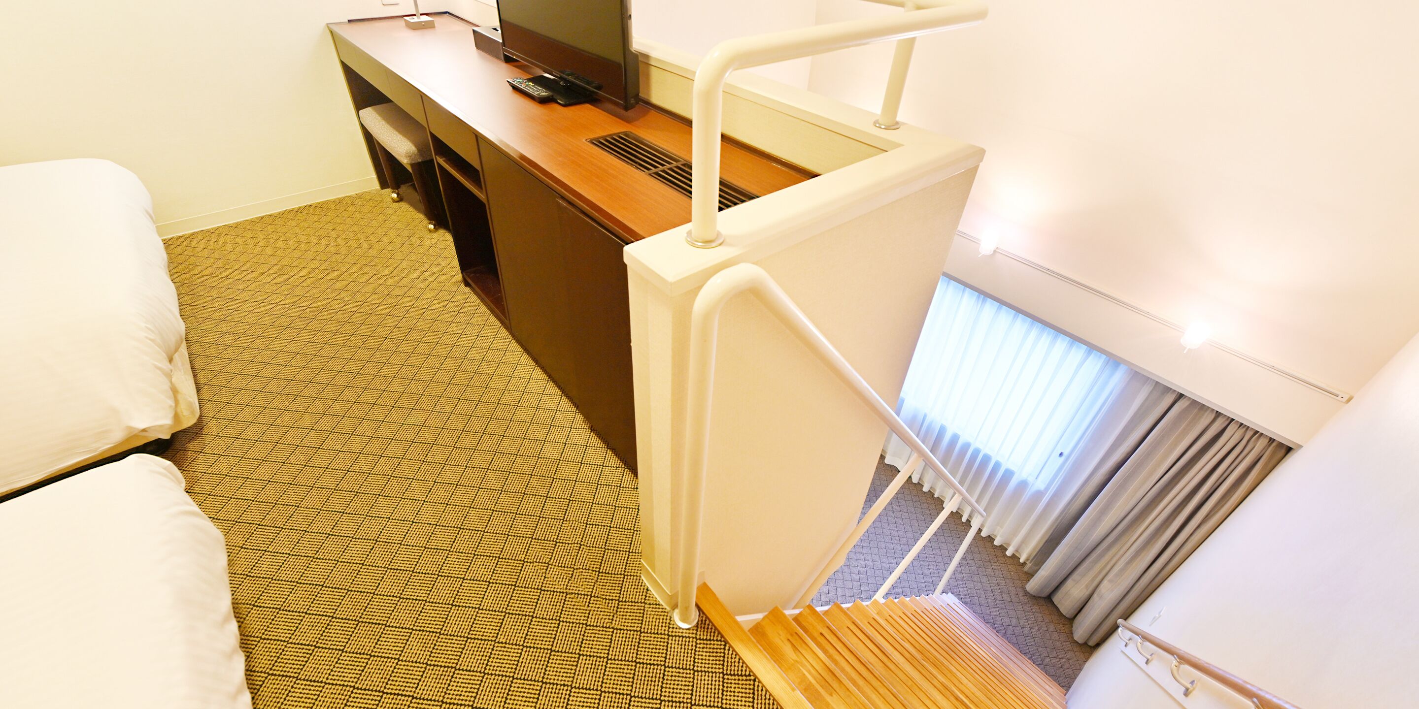A hotel room with a bed, a desk with a computer, and a staircase.