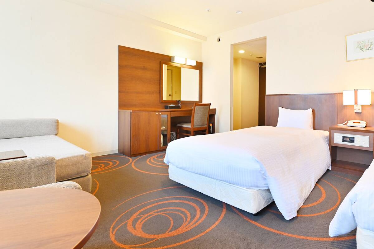 A hotel room with two beds, a desk, a chair, and a sofa.