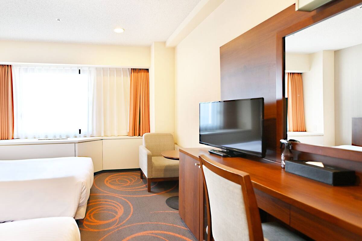 A hotel room with a bed, a desk, a TV, and a chair.