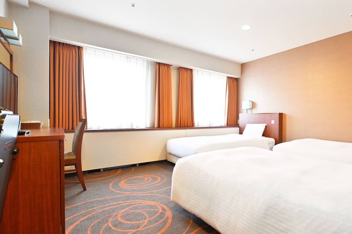 A hotel room with two beds, a desk, a chair, and a window with curtains.