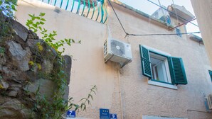 Un bâtiment avec un mur en pierre, un balcon en métal et une fenêtre avec des volets verts.