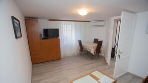 Une pièce avec une armoire en bois, un téléviseur posé sur le dessus, une table à manger avec des chaises et un tableau d’affichage où sont accrochés des papiers.
