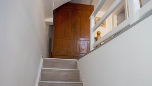 Un escalier avec des marches en bois et des murs blancs, menant à une porte en bois située en haut.