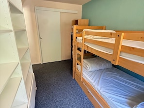 Une chambre avec un lit superposé, une porte et une étagère blanche.