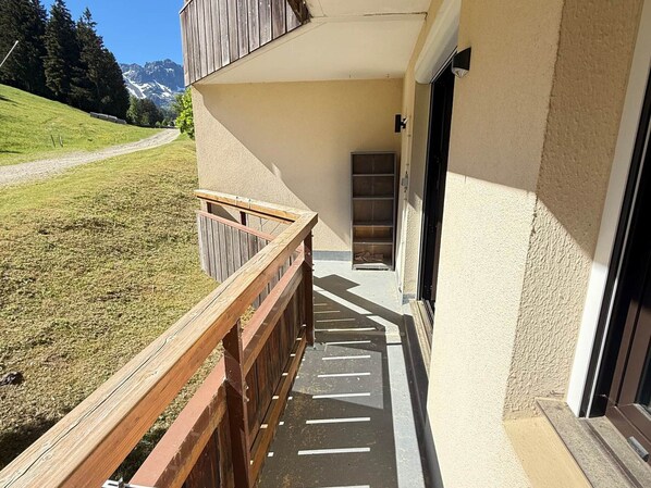 A building with a wooden deck, a door, and a view of a grassy area with mountains in the background.