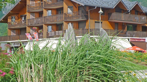 Ein mehrstöckiges Holzchalet mit Balkonen vor einer Bergkulisse.