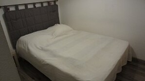 Ein kleines Zimmer mit einem Einzelbett, einem schlichten Kopfteil und einer schlichten Wand.