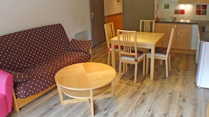 Ein gemütlicher Wohnbereich mit Sofa, Esstisch und Stühlen. Eine kleine Küchenzeile mit Mikrowelle und Schränken ist zu sehen.