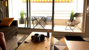 A living room with a sofa, a coffee table with bowls and a bottle, and a sliding glass door leading to an outdoor patio with a table and chairs. - Modern sea-facing apartment with garage and free WiFi (Les Sables-d'Olonne)