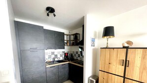 A compact kitchen with dark cabinets, a tiled backsplash, a small sink, and a trash bin. - Modern sea-facing apartment with garage and free WiFi (Les Sables-d'Olonne)