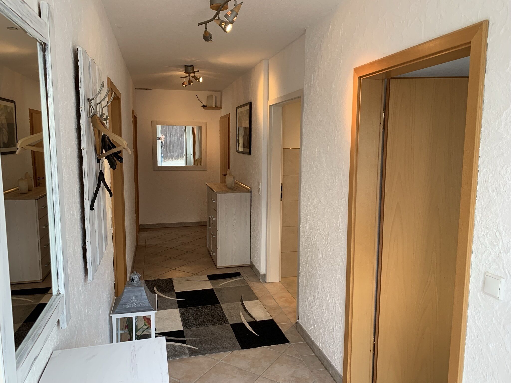A hallway with a checkered floor, a wooden door on the right, and a mirror on the left.