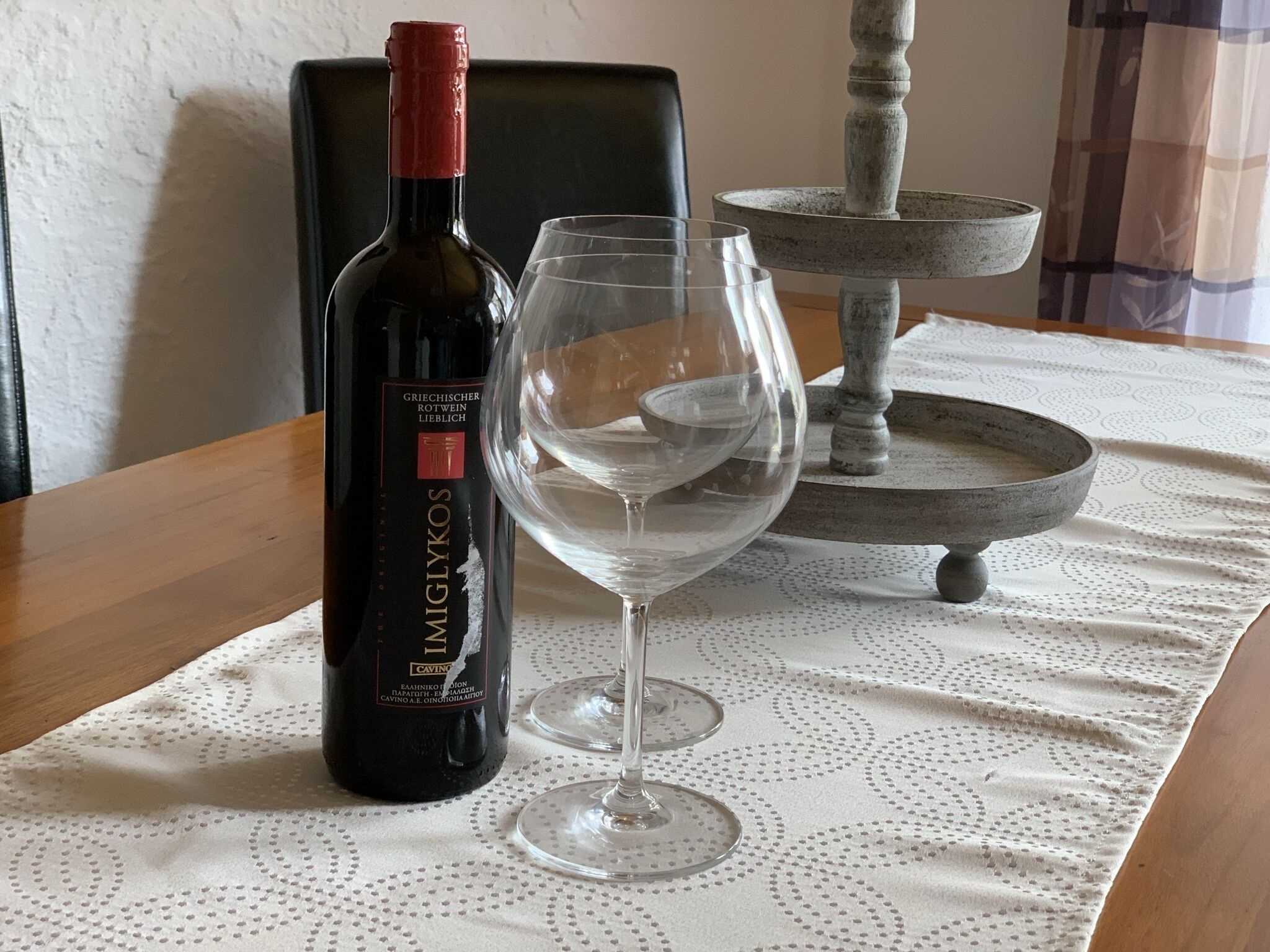 A bottle of wine and an empty wine glass on a table with a lace tablecloth.