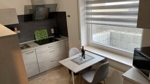 Ett kompakt kök med en matplats, en inbyggd spis, ett fönster med persienner och ett element.