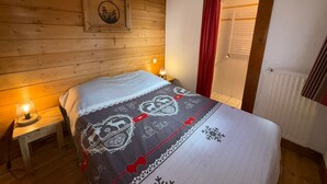 A wooden-paneled room with a bed, a nightstand with a lamp, a framed picture on the wall, and a window with red curtains. - T3 Apartment in Les Saisies, 6 people, parking included (Les Saisies)