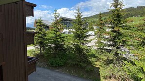 A wooden building with a balcony overlooking a modern building with glass windows, surrounded by evergreen trees and a clear sky. - T3 Apartment in Les Saisies, 6 people, parking included (Les Saisies)