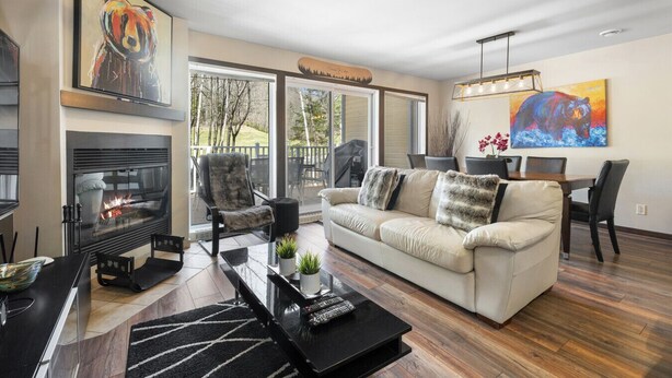 Een moderne woonkamer met een open haard, een bank, een eettafel en een groot raam.