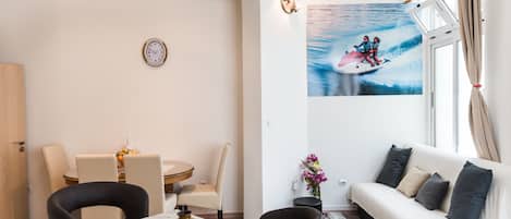 A modern living room with a dining area, a sofa, a coffee table, and a wall-mounted clock.