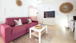 Un saló modern amb un sofà rosa, una taula de centre blanca, una televisió de pantalla plana, una làmpada al sostre i una escala.