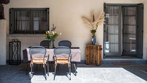 Un patio exterior amb una taula i cadires, un vas amb flors i un armari de fusta.