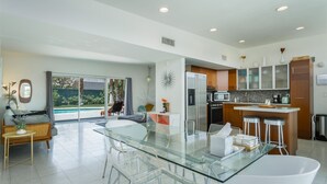 Une cuisine moderne dotée d’un îlot central, d’un coin repas avec des tables en verre et d’une vue sur une piscine.