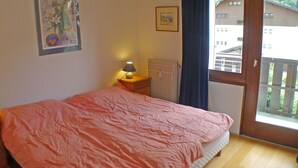 A bedroom with a bed, a nightstand, a lamp, a radiator, and a window with a view of buildings outside. - 4-room duplex with balcony and Wifi in Samoëns for 8 guests (Samoëns)