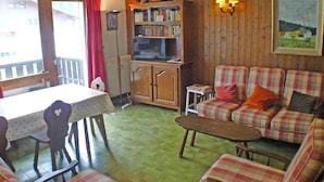 A cozy living room with a checkered sofa, a wooden cabinet with a television, a dining table with chairs, and a bookshelf. - 4-room duplex with balcony and Wifi in Samoëns for 8 guests (Samoëns)