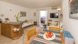 A cozy living area with a dining table set for two, a kitchen area with a wooden counter, and a view of the sea through an open door. - Pirka - Apt. w. Terrace & sea View,2 min to Beach (Sutivan)