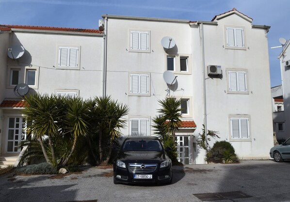 Un bâtiment à deux étages, doté d’antennes paraboliques, avec une voiture garée devant et des palmiers.