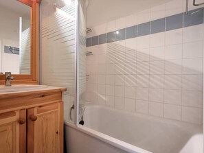 A bathroom with a wooden vanity, a mirror, a bathtub, and tiled walls.