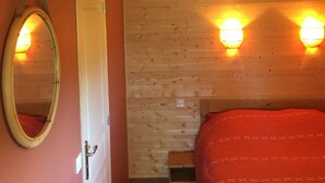 A bedroom with a wooden ceiling, a bed with a red blanket, a mirror, and two wall-mounted lights. - Chalet - Lac Daydat (Aydat)