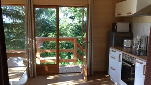 A wooden cabin with a kitchen, dining area, and a deck with a view of trees. - Chalet - Lac Daydat (Aydat)