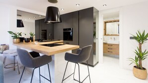 A modern kitchen with a central island, two bar stools, a built-in oven, and a large pendant light. - Beautiful, Modern Apartment Near the Sea, Croatia (Kastela)