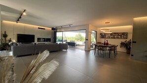 Ein modernes Wohnzimmer mit grauem Sofa, einem Flachbildfernseher und einem Essbereich mit Tisch und Stühlen.