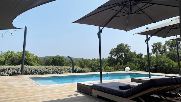 Eine Holzterrasse mit Pool, Liegestühlen und Sonnenschirmen.