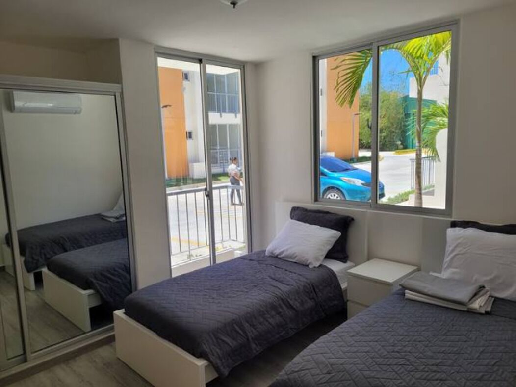 A hotel room with two beds, a sliding glass door to the balcony, and a view of the street and palm trees outside.