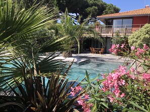 A pool area with a small waterfall, surrounded by lush greenery and pink flowers. - Villa, pool, 200 m from Eyrac Beach, south-facing terrace, like a lodge. (Arcachon)