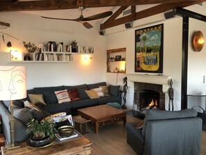 Een gezellige woonkamer met een open haard, een plafondventilator en een boekenplank vol boeken.