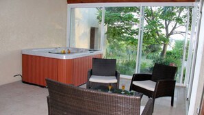 Ein Balkon mit Korbmöbeln, einem Whirlpool und Blick auf Grünflächen.