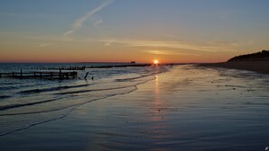 A beach at sunset with a wooden pier extending into the water.
