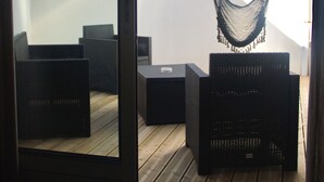 An open sliding door to a room with a wooden deck, a hanging hammock, and black wicker furniture.
