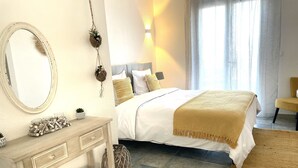 Un dormitorio con cama, mesita de noche, espejo y ventana con cortinas.