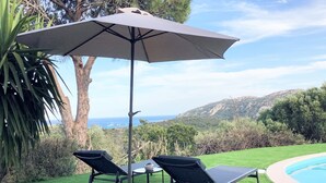 Un área junto a la piscina con dos sillas reclinables, una mesa y una sombrilla.