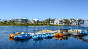 A marina with several colorful pedal boats docked, a dock extending into the water, and buildings in the background. - Surf's Up at Island Breeze of CB (Carolina Beach)