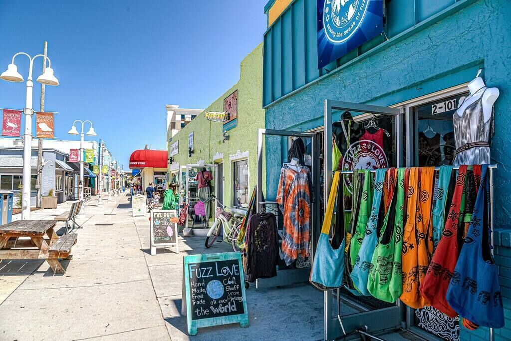 A street with outdoor seating, a store named 'Fuzz Love' selling handmade items, and a clear blue sky.