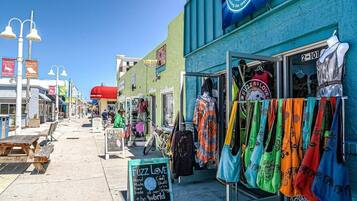 A street with outdoor seating, a store named 'Fuzz Love' selling handmade items, and a clear blue sky.