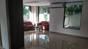 A spacious room with a large window, a red leather sofa, a glass coffee table, and a tiled floor.