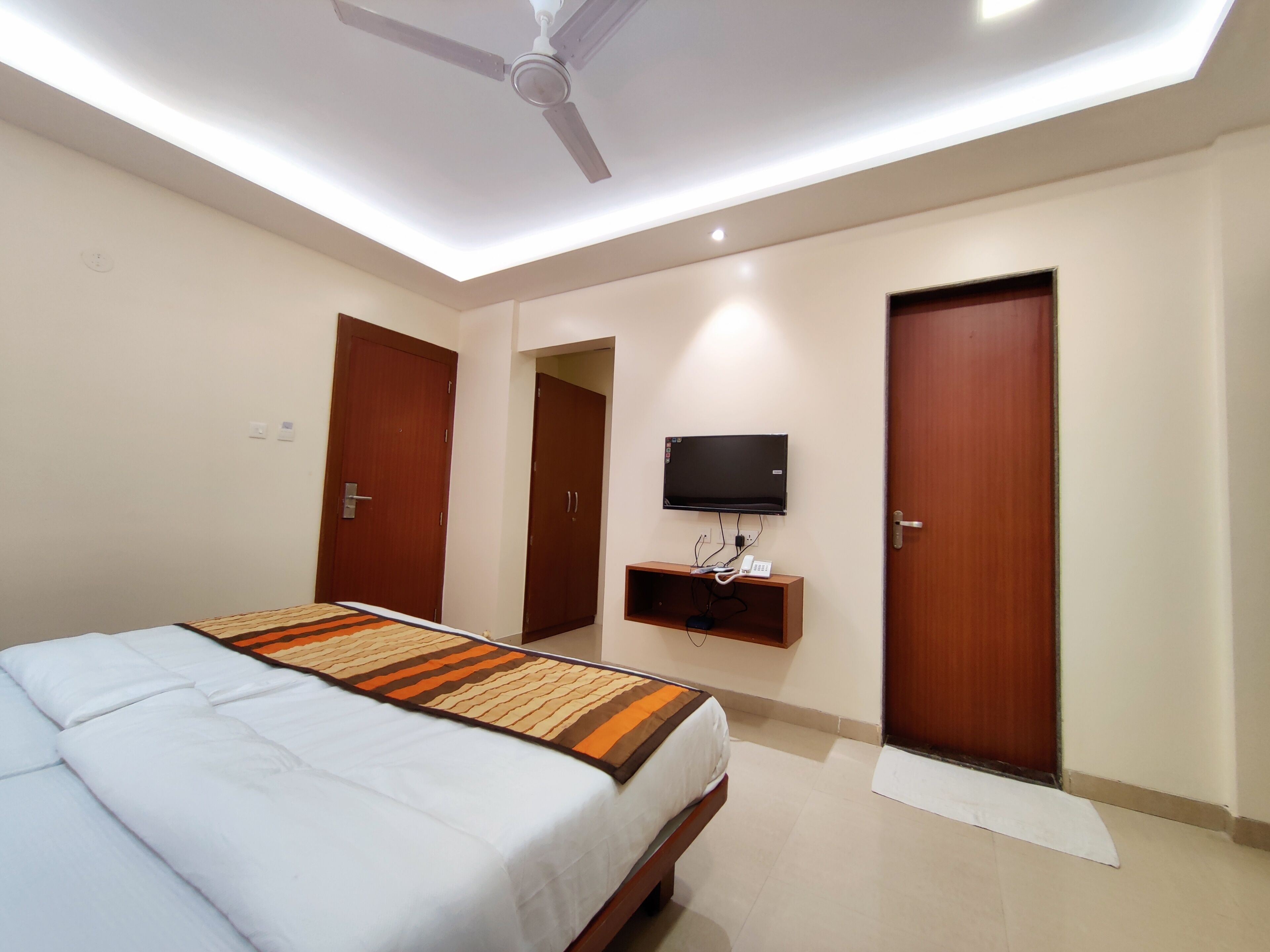 A hotel room with a bed, a ceiling fan, a TV, and two doors.