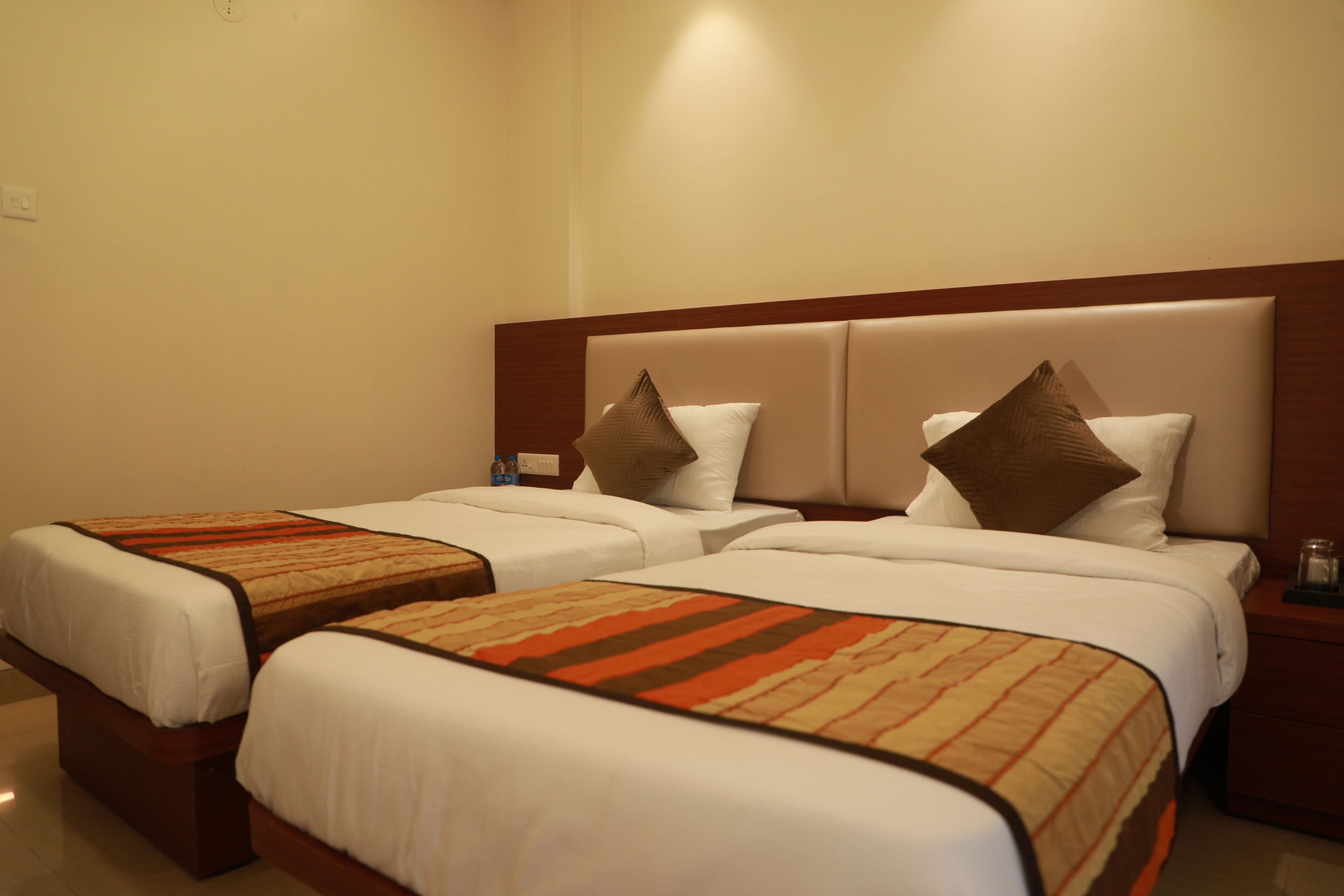 Habitación de hotel con dos camas, cada una con cabecero, ropa de cama blanca y una manta estampada.
